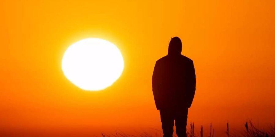 Ein Spaziergänger geniesst am Strand von Schillig in Niedersachsen den Sonnenaufgang. Foto: Sina Schuldt/dpa