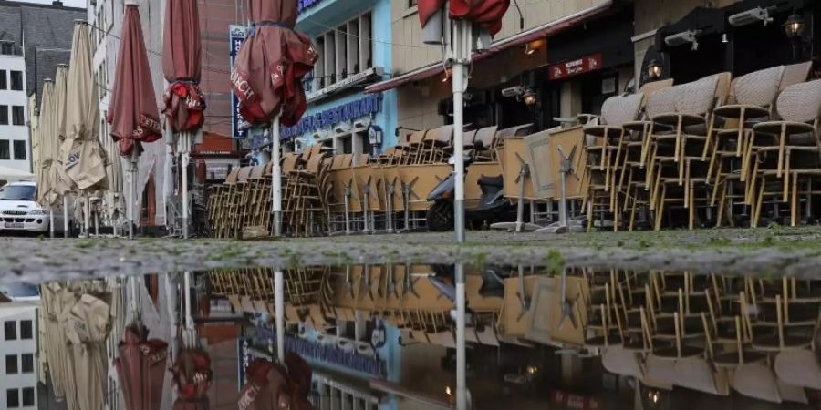 Zusammengestellte Tische und Stühle vor einem geschlossenen Lokal in Köln. Foto: Oliver Berg/dpa