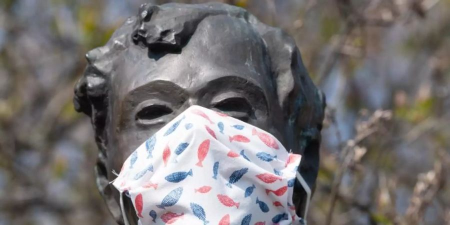 Eine selbstgebastelte Mundschutzmaske über der Kästner-Bronzeplastik in Dresden. Ingenieuren zufolge haben Staubsaugerbeutel für eine Maske der Marke Eigenbau hervorragende Filtereigenschaften. Foto: Sebastian Kahnert/dpa-Zentralbild/dpa
