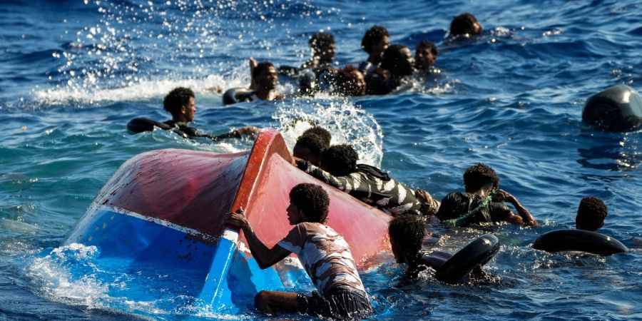 Migranten schwimmen neben ihrem umgestürzten Holzboot im Mittelmeer (Archiv).