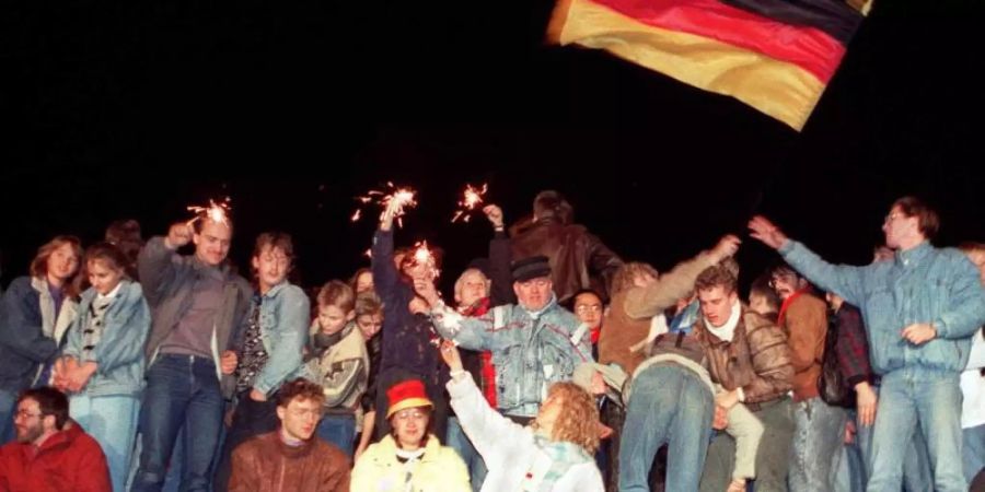 Mit Wunderkerzen in den Händen freuen sich die Menschen auf der Berliner Mauer über die Öffnung der deutsch-deutschen Grenzen. Foto: DB/dpa