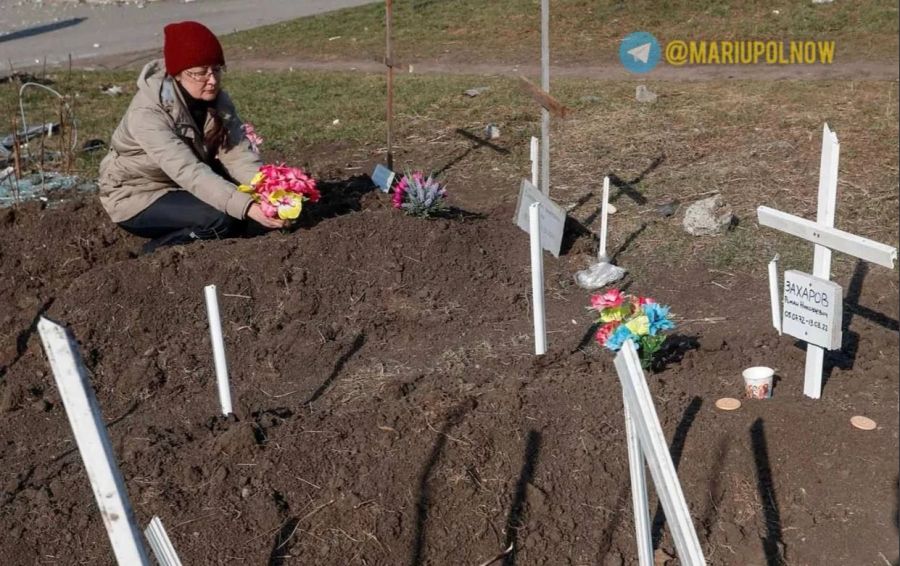 Eine Frau legt bei einem provisorischen Grab in Mariupol Blumen nieder.