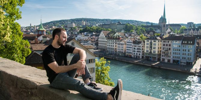 Mann sitzt auf Stadtmauer mit Blick auf Zürich.