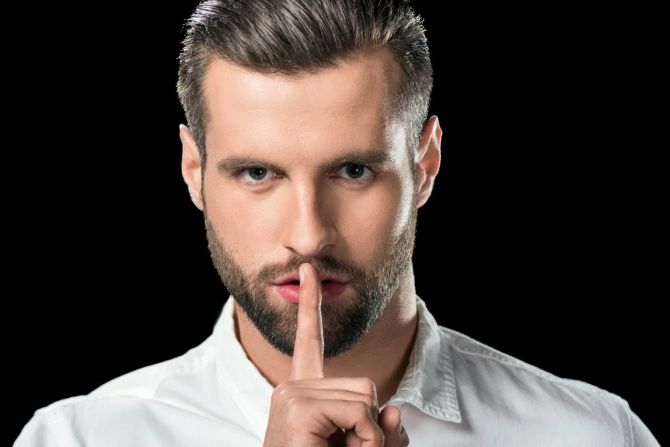 junger mann hält sich zeigefinger vor den mund, schwarzer hintergrund