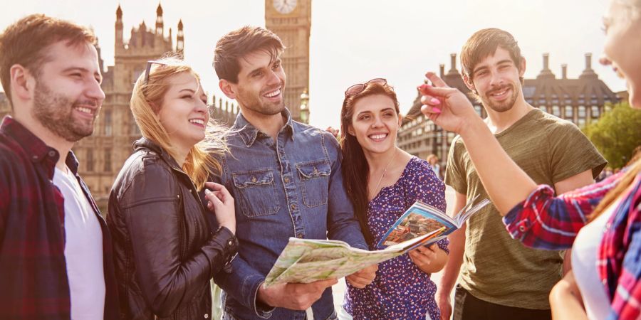 Gruppe junger Menschen vor dem Big Ben in London mit einer Landkarte und einem weiblichen Guide.