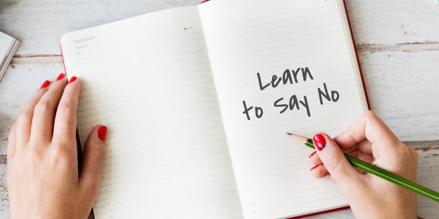 Frau schreibt Notizen ins Tagebuch: learn to say no.