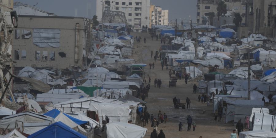 dpatopbilder - Palästinenser gehen im Regen eine Straße mit zerstörten Gebäuden entlang. Foto: Jehad Alshrafi/AP/dpa