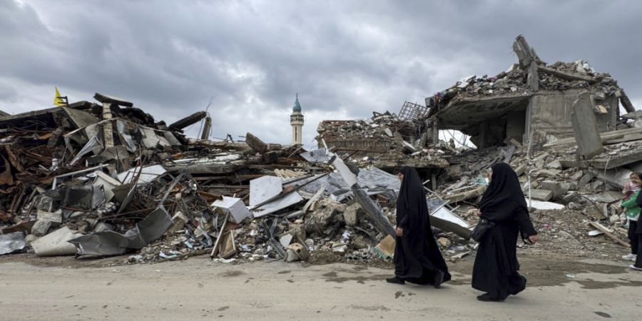 ARCHIV - Einwohner gehen an zerstörten Gebäuden im Libanon vorbei (Archivbild). Foto: Bassam Hatoum/AP/dpa