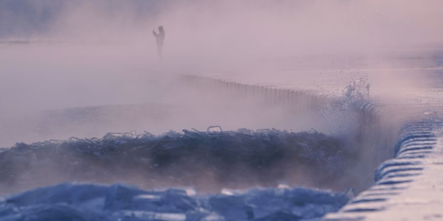Eine Person spaziert über einen mit Eis bedeckten Strand am Ufer des Michigansees. Foto: Kiichiro Sato/AP/dpa