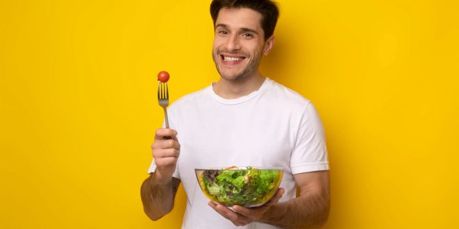 Fröhlicher Mann isst Salat.