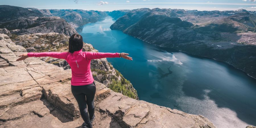 Frau au den Klippen mit Blick auf die norwegischen Fjorde.