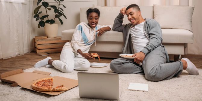 Mann, Frau im Wohnzimmer auf dem Boden, Pizza essend und Film auf dem Laptop schauen