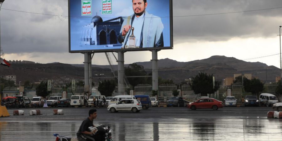 ARCHIV - Fahrzeuge fahren an einem Banner des Huthi-Führers Abdel Malik al-Huthi vorbei. Foto: Osamah Abdulrahman/AP/dpa/Archivbild