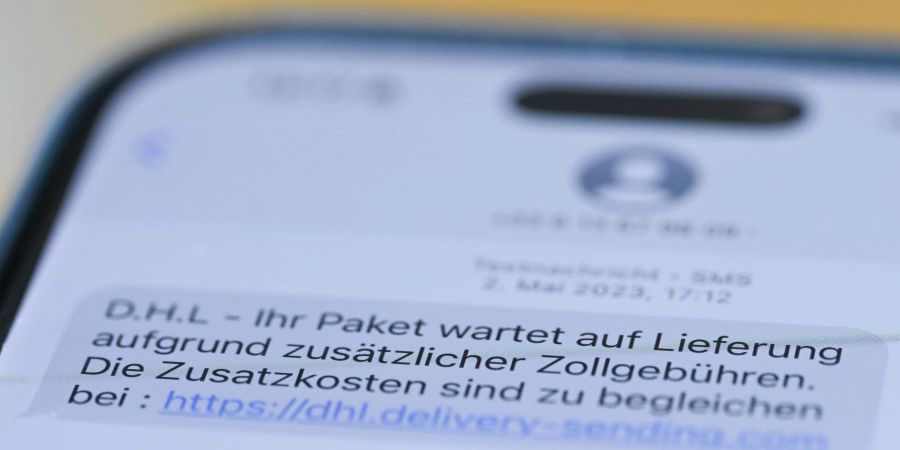 Auf einem Smartphone ist eine Betrugs-SMS zu lesen, in der Kriminelle ein Paket ankündigen und dafür Zollgebühren einfordern.