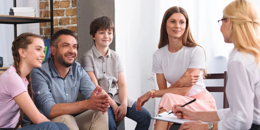 Glückliche Familie sitzt auf Therapiesitzung von weiblichen Berater Schreiben in Klemmbrett im Büro.