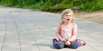 Wütendes kleines Mädchen sitzt auf dem Boden und schreit.