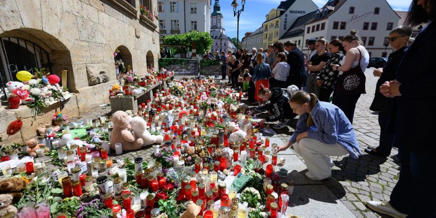 Menschen stehen am Rande eines Gottesdienstes für die getötete Valeriia in Döbeln vor Blumen und Kerzen.