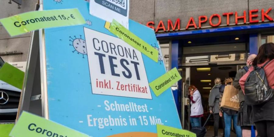 Passanten stehen in der Münchner Innenstadt vor einer Apotheke, die Coronatest für 15 Euro anbietet. Foto: Peter Kneffel/dpa