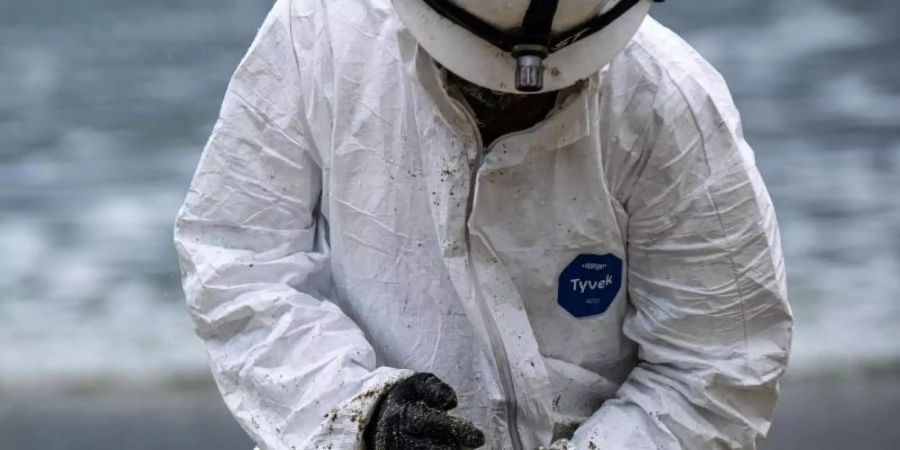 Ein Arbeiter in einem Schutzanzug säubert einen Strandabschnitt. Foto: Jason Ryan/ZUMA Press Wire Service/dpa