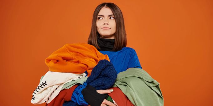 Oft fällt es schwer, das Ausmisten im Kleiderschrank anzugehen. Mit einem sinnvollen Plan kann es ganz gut klappen. Frau mit vieler Kleidung