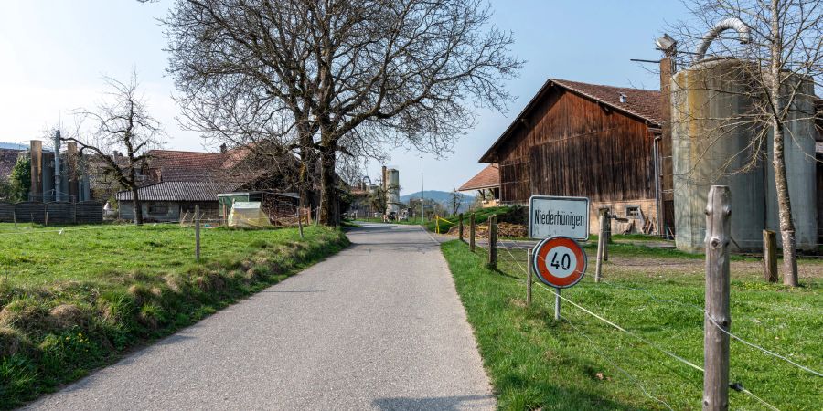 Die Ortstafel von Niederhünigen an der Kalchofenstrasse. Im Hintergrund Bauernhäuser und Silos.