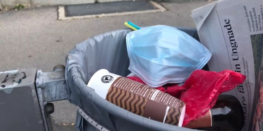 Eine Schutzmaske liegt ganz oben im Abfall an einer Berner Busstation. Ein Windstoss und die Maske liegt auf der Strasse.