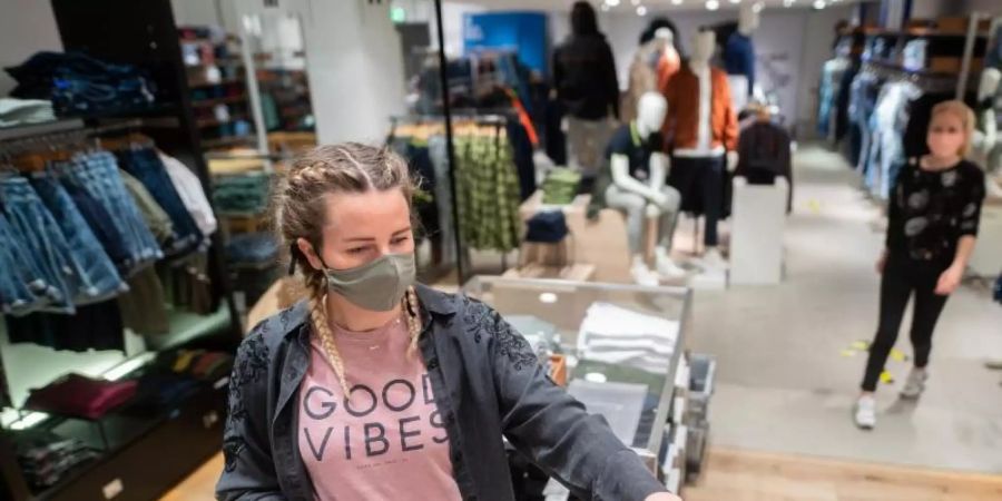 Eine junge Frau trägt in einem Bekleidungsgeschäft in Hamburg einen Mund- und Nasenschutz. Der von den Grünen vorgeschlagene Gutschein soll im stationären Handel, für stationäre Dienstleistungen oder in der Gastronomie eingelöst werden können. Foto: Daniel Reinhardt/dpa