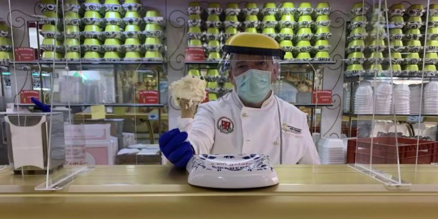 Paolo Costantini serviert mit Schutzausrüstung in seiner römischen Eisdiele „Il Gelatone“ Eis. Foto: Annette Reuther/dpa