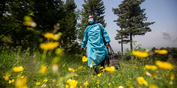 Eine Mitarbeiterin des Gesundheitswesens trägt während einer Impfaktion gegen das Coronavirus eine Tasche mit Impfdosen über eine Wiese. Coronavirus - Indien