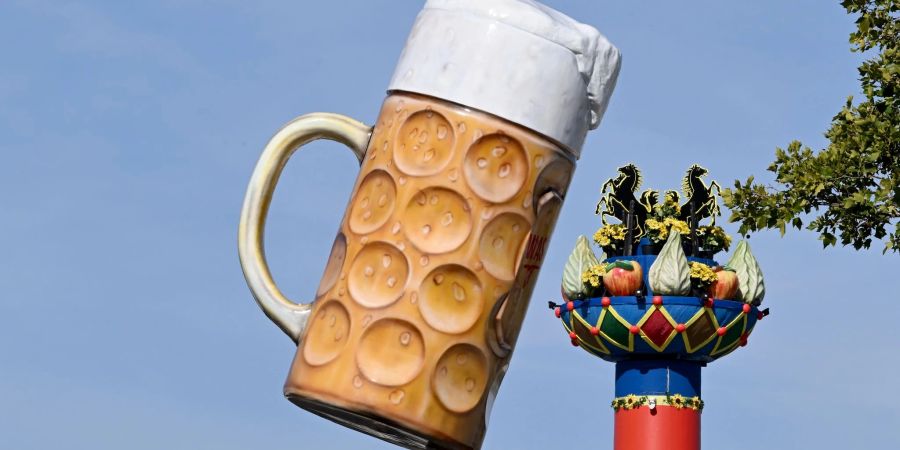 Ein riesiger Bierkrug steht am Eingang auf dem Festgelände Cannstatter Wasen, im Hintergrund steht die Fruchtsäule.