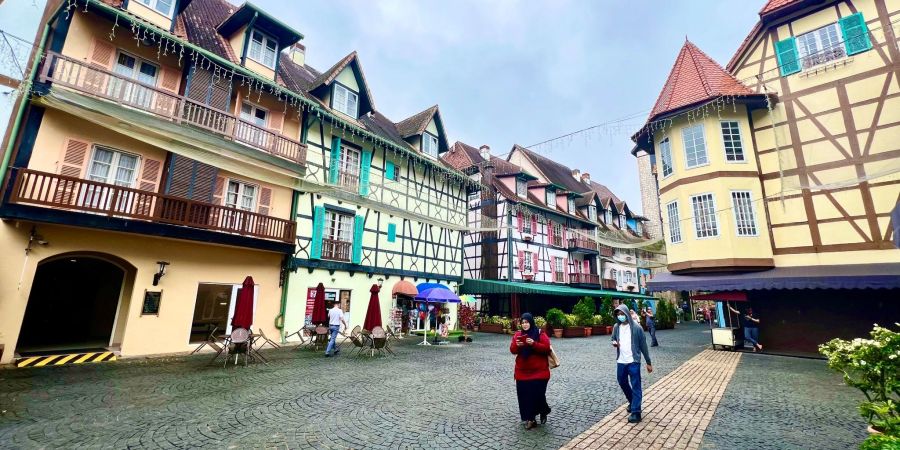Besucher schlendern über das Kopfsteinpflaster durch Colmar Tropicale, vorbei an Fachwerkhäusern mit Türmchen, Erkern und bunten Fensterläden.