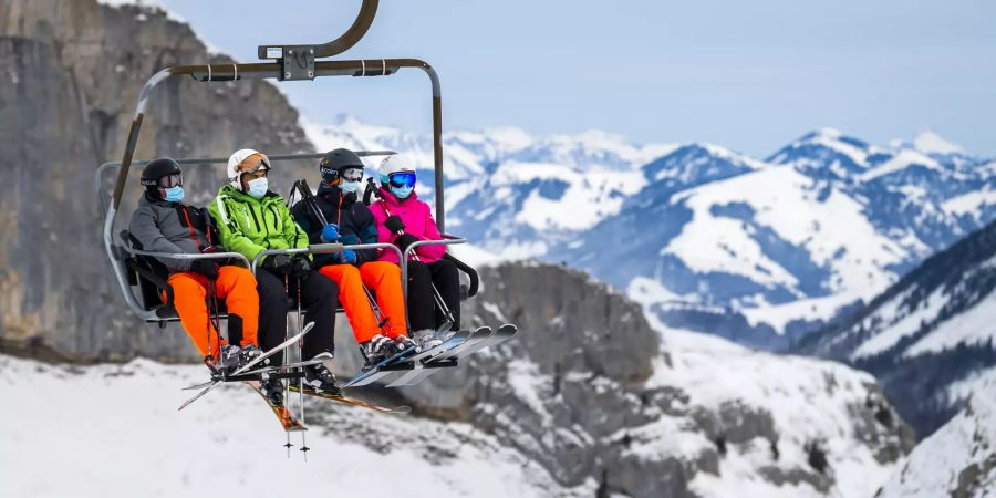 Skifahrer sitzen auf dem Lift. Wegen des Coronavirus tragen sie alle Masken.