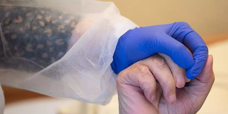 Eine Altenpflegerin in Schutzausrüstunghält die Hand eines Bewohners. Foto: Sebastian Gollnow/dpa
