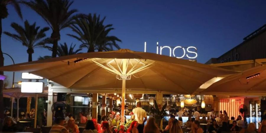 Menschen sitzen in einer Bar an der Strandpromenade von Palma. Foto: Clara Margais/dpa