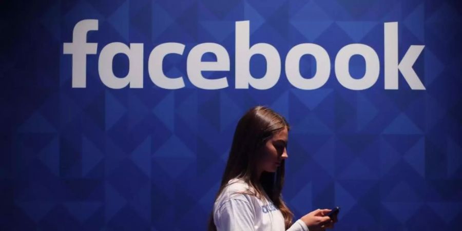 Eine Frau steht mit ihrem Smartphone unter dem Facebook-Schriftzug. Foto: Niall Carson/PA Wire/dpa