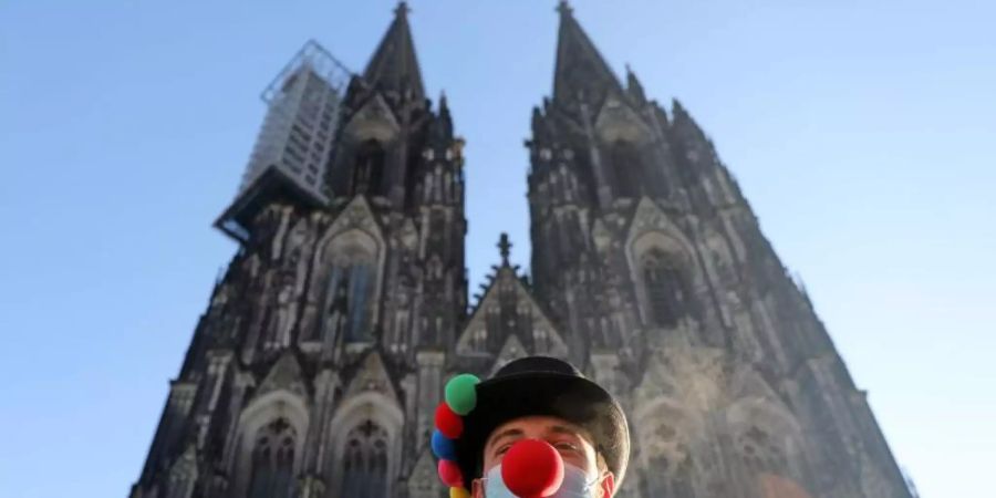 Lorenz steht mit Clownsnase auf der Maske vor dem Kölner Dom. Foto: Oliver Berg/dpa