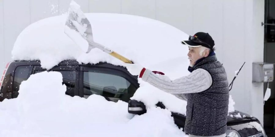Völlig bedeckt von Neuschnee: Ein Mann in Fukui schaufelt sein Auto frei. Foto: --/kyodo/dpa