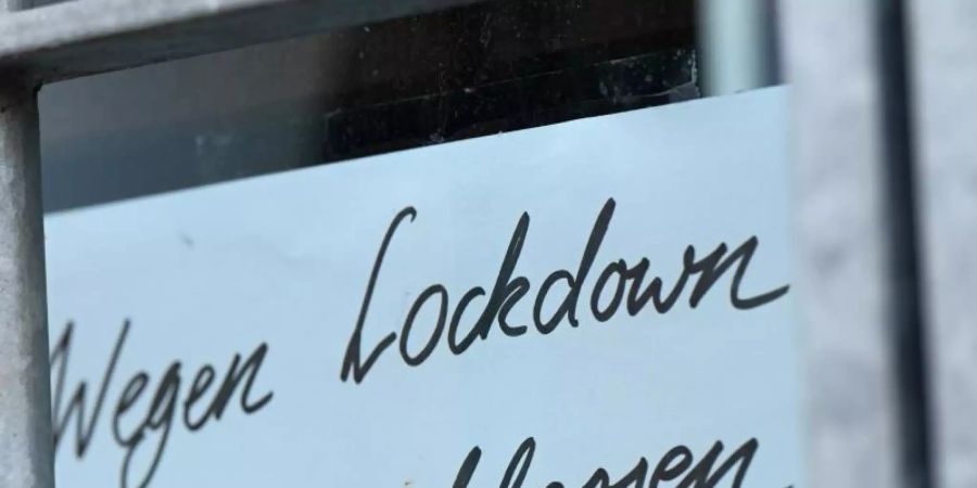 Ein Zettel mit der Aufschrift «Wegen Corona geschlossen» hängt am Schaufenster eines Geschäfts. Foto: Arne Dedert/dpa