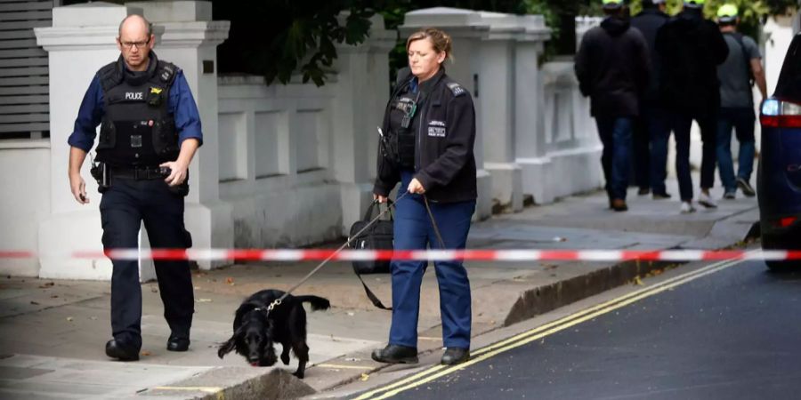 Zwei Polizeibeamte laufen mit einem Hund die Umgebung ab, wo der Bombenanschlag in London ausgeführt wurde.