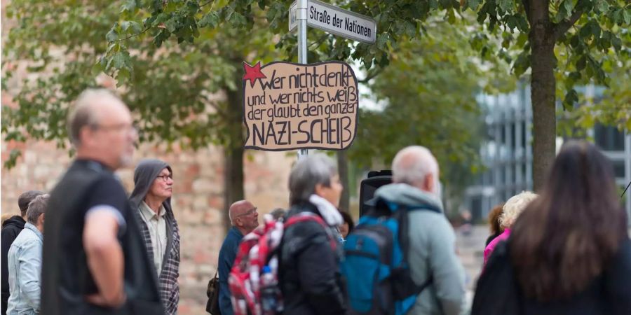 Ein Schild mit der Aufschrift «Wer nicht denkt und wer nichts weiss, der glaubt den ganzen Nazi-Scheiss» hängt an einem Strassenschild, während mehrere Personen der Kundgebung der Chemnitzer Friedensgruppen am Roten Turm folgen.