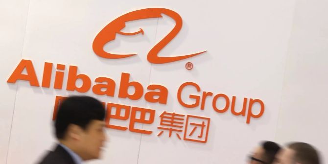 Menschen laufen am Logo von Alibaba vorbei.