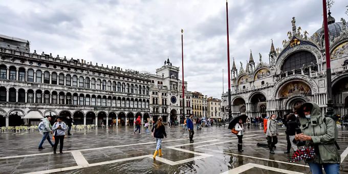 Passanten gehen bei Regen über den Markusplatz. Venedig