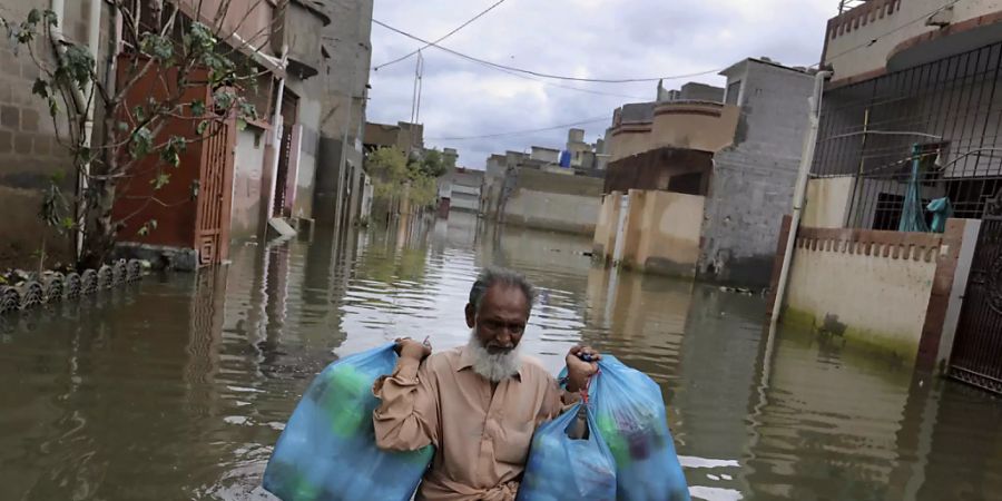 Ein Mann trägt Waren, während er nach heftigen Regenfällen durch eine überflutete Strasse watet. Nach Überschwemmungen in Pakistans Millionenstadt Karatschi sind in den vergangenen drei Tagen mindestens 41 Menschen ums Leben gekommen. Foto: Fareed Khan/AP/dpa