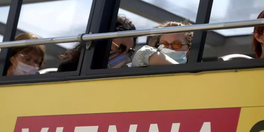 Menschen sitzen in einem Touristenbus und tragen Gesichtsmasken. 3600 der aktuell rund 6600 aktiven Fälle in Österreich werden aus Wien gemeldet. Foto: Ronald Zak/AP/dpa