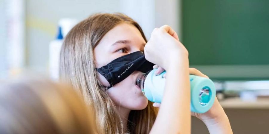 Eine Schülerin der Klasse 8a der Gesamtschule in Münster, hebt ihre Mund- und Nasenmaske an um etwas zu trinken. Foto: Guido Kirchner/dpa