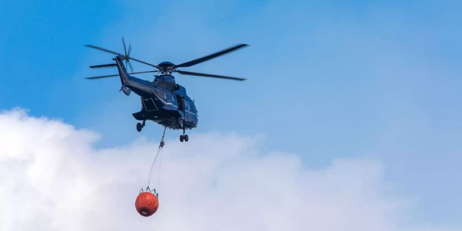 Ein Helikopter der Bundespolizei transportiert Löschwasser zu einem Brandherd in der Nähe der evakuierten Ortschaft Alt Jabel.