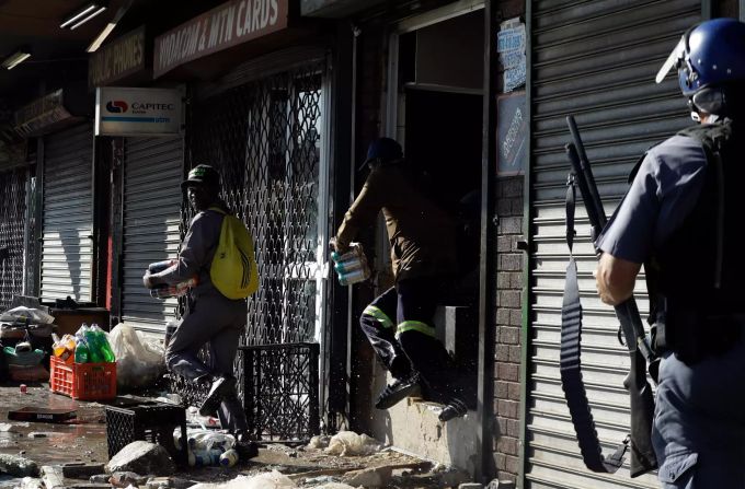 Plünderer machen sich mit Waren aus einem Geschäft davon, als sich ein Bereitschaftspolizist in Germiston östlich von Johannesburg nähert. Südafrika