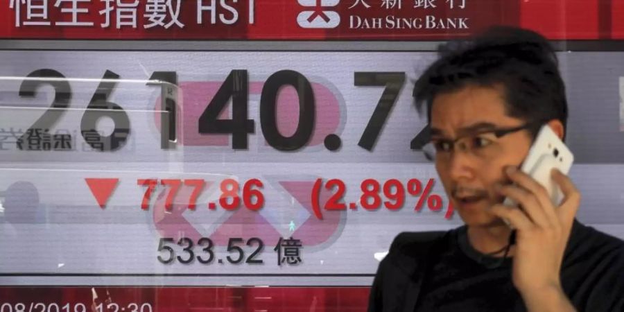 Ein Mann telefoniert in Hongkong vor einer Anzeigetafel mit dem Hong Kong Composite Index. Foto: Kin Cheung/AP