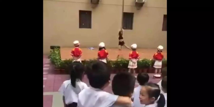 Screenshot aus dem Twittervideo eines betroffenen Elternteils. Pole-Dancerin performt auf der Bühne, Kinder in Uniform stehen davor und schauen zu.