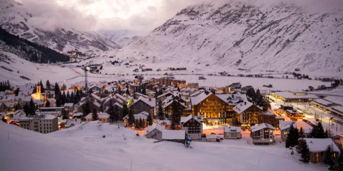 Das Dorf Andermatt vor dem Urserntal ist winterlich eingeschneit und beleuchtet.